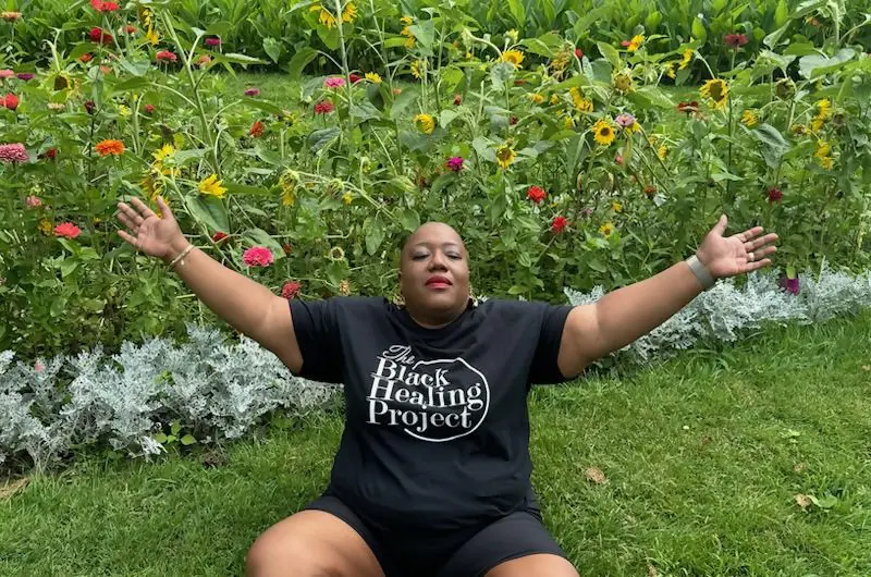 Person sitting with arms raised in garden.